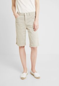 Vaaleanbeiget polvipituudet shortsit, jotka on valmistettu puuvillasta. Niissä on klassinen vyötärönauha, etutaskut ja käännetyt lahkeet. Yhdistetty valkoisiin slip-on-kenkiin.