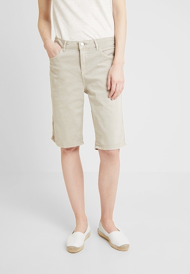 Vaaleanbeiget polvipituudet shortsit, jotka on valmistettu puuvillasta. Niissä on klassinen vyötärönauha, etutaskut ja käännetyt lahkeet. Yhdistetty valkoisiin slip-on-kenkiin.