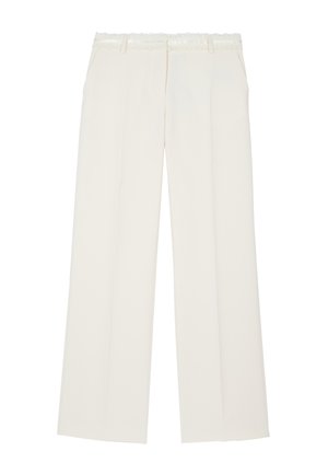 Mujer negra vistiendo un traje a medida color blanco roto con ribete de encaje en los puños y el escote de la chaqueta, combinado con sandalias negras de punta abierta.