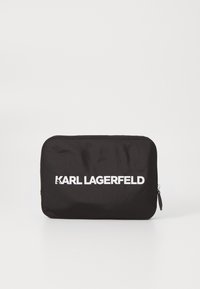 Juodas nailono maišelis su lygiu paviršiumi, ant kurio priekyje yra balta logo „KARL LAGERFELD“, o šone yra užtrauktukas.