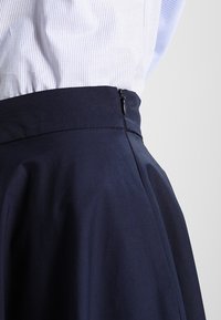 Jupe A-line marine à texture lisse, dotée d'une taille ajustée et d'un détail de fermeture à glissière sur le côté.