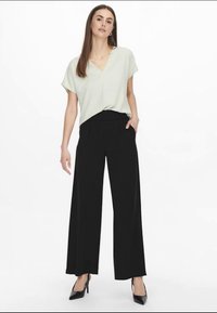 Jasnozielona bluzka z dekoltem w serek i luźnym krojem, zestawiona z czarnymi spodniami o szerokich nogawkach i wysokim stanem. Całość dopełniają czarne szpilki.