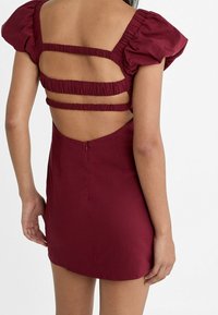 Bordeauxkurzes Kleid mit Puffärmeln, das einen ausgeschnittenen Rücken und drei horizontale Riemendetails aufweist. Glattes Material mit einem Reißverschluss.