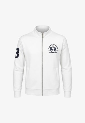 Giacca bianca con zip e colletto alto, con logo del giocatore di polo blu navy sul petto e numero 3 sulla manica destra.
