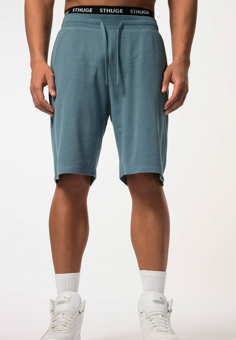 Turquoise shorts met een elastische tailleband, voorzien van een zwart "STHUGE" logo en twee zijzakken. Zachte, textuurstof, knie-lange ontwerp.