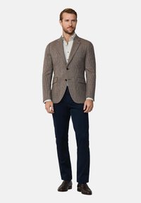 Blazer marrone a motivo houndstooth con rever a punta, due bottoni frontali e tasche a toppa, abbinato a una camicia a scacchi chiara e pantaloni scuri.
