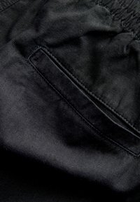 Juodas audinys su lygiu paviršiumi ir elastinga juosta. Įrengtas pleištinis kišenė su subtilia siuvimo detale.