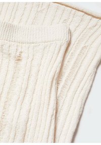 Ecrufarbene, gerippte Stricksocken, auf einem weißen Hintergrund gefaltet, zeigen Textur und Details des elastischen Bündchens.