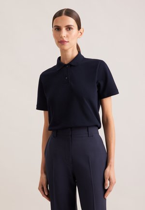 Navy polo shirt with short sleeves, three-button placket, and a textured fabric. Paired with tailored dark trousers.
