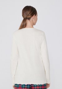 Camisa de algodón crema de manga larga con cuello redondo y dobladillo con forma de cascada, combinada con pantalones de cuadro.