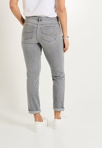Jeans de mezclilla gris con un ajuste tapered, puños enrollados y dos bolsillos traseros con detalles de costura. Llevados con zapatillas blancas.