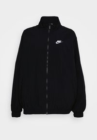 Svart Nike vindjacka med hög krage, hel dragkedja fram, elastiska muddar och en vit broderad logotyp på vänster bröst.