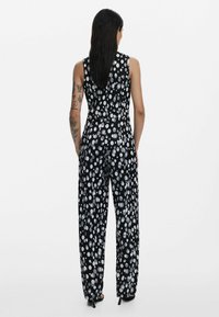 Svart byxdress med vita prickar, ärmlös design, vida ben, mjukt tyg och figurnära midja.