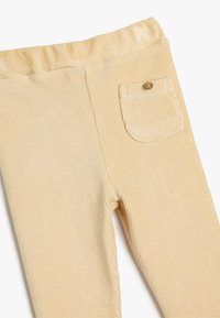 Cremefarvede ribbet cordbukser med elastisk talje og en enkelt knaplukket baglomme. Blød struktur og tætsiddende design.