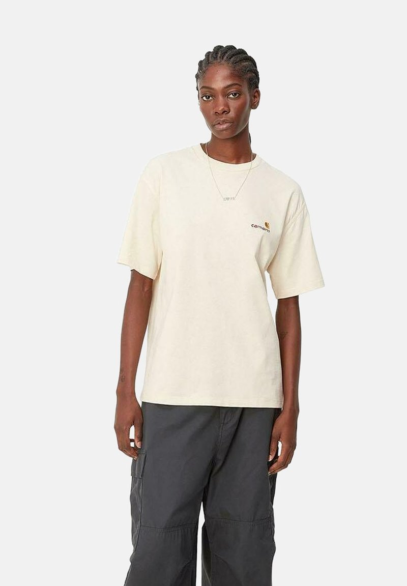 T-shirt en coton couleur crème avec un col rond, des manches courtes et un détail de logo brodé sur la poitrine gauche. Associé à un pantalon cargo noir.