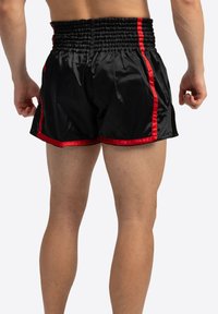Sorte satin sportshorts med røde sidelister, elastisk talje og slids i kanten for fleksibilitet. Let glans på den glatte tekstur.