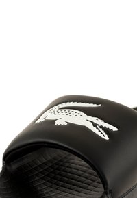 Infradito nere con un grande logo di coccodrillo bianco sulla fascia superiore, realizzate in materiale sintetico liscio con una soletta testurizzata.