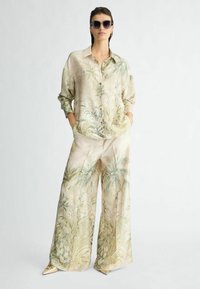 Zijden blouse en bijpassende wijde broek in een lichtbeige toon met een palmbladerenprint; heeft een kraag, knoopsluiting aan de voorkant en zijzakken.