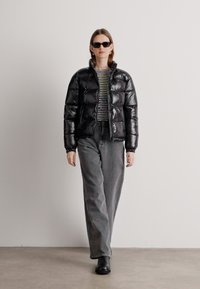 Melna pūkaina jaka, mirdzošs materiāls, ar rāvējslēdzēju priekšā, garām piedurknēm, apvienota ar pelēkiem platiem biksēm un svītrainu blūzi. Melni saulesbrilles papildina izskatu.