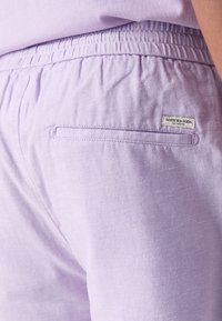 Gaiši violeta bikses ar elastīgu jostasvietu, aizmugures kabatu un mazu Scotch & Soda etiķeti. Materiāls ir mīksts ar teksturētu virsmu.