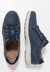 Marinblå lädersneakers med perforerade detaljer, rund tå, snörningsdesign, vadderad ljusbrun innersula och en vit gummisula med brun friktion.