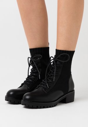 Bottines noires avec une combinaison de cuir lisse et de tissu texturé. Fermeture à lacets à l'avant, bout rond et semelle en caoutchouc épaisse.