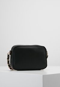 Mustikka musta ristikkokassi, joka on valmistettu teksturoidusta keinonahasta. Varustettu kultaisella ketjuhihnalla ja vetoketjulla suljettuna. Yksinkertainen muotoilu.