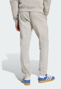 Šedé tepláky s elastickými manžetami a bočnými vreckami, v kombinácii s modro-bielymi teniskami s tromi pruhmi a pieskovou podrážkou.