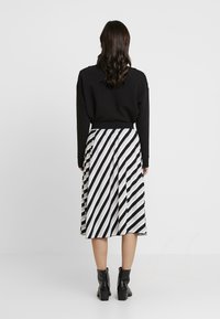 Pull noir à manches longues associé à une jupe de longueur genoux avec un motif de rayures diagonales noir et blanc. Bottines noires.