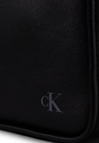 Borsa in pelle nera con texture, caratterizzata da un logo embosso "cK" in grigio, con un design elegante e minimalista e linee pulite.