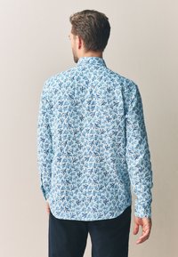 Vaaleansininen paita, jossa tummansininen korallikuvio, normaali istuvuus, pitkät hihat, napillinen kaulus. Sileä kangas, kaareva helma, rento muotoilu.