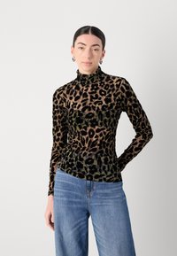 Langstaande, hooge hals top met een transparant luipaardpatroon in bruin en zwart. Getextureerde stof met een getailleerde silhouet, gecombineerd met blauwe spijkerbroeken.