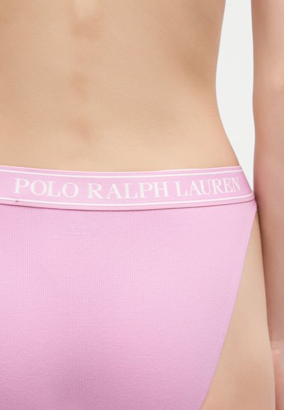Κοντινό πλάνο της κάτω μέσης ενός ατόμου που φοράει ροζ εσώρουχα με λευκή ζώνη μέσης με το λογότυπο Polo Ralph Lauren.