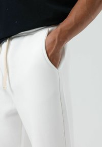 Witte joggingbroek met een gladde textuur, zijzakken en een tailleband met trekkoord. Ontworpen voor comfort met een losse pasvorm.