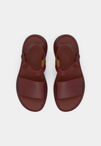 Κόκκινα συνθετικά σανδάλια με δύο φαρδιές λουρίδες και ρυθμιζόμενο λουράκι στον αστράγαλο. Λείο υφή και επίπεδα λαστιχένια πέλματα.