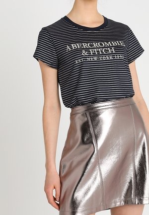 Persoon in een zwart-wit gestreept Abercrombie & Fitch t-shirt, ingestopt in een glanzende metallic zilveren minirok.