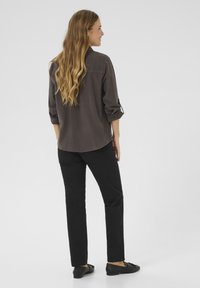 Donkergrijs shirt met opgerolde mouwen, een ronde zoom en geborduurde details op de achterkant, gecombineerd met zwarte rechte broeken en zwarte flats.