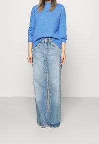 Pull en maille bleu avec un col montant et des manches longues, associé à un jean bleu clair à jambes larges avec un effet délavé et des poches avant.