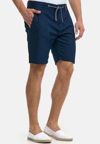 Marineblaue Baumwollshorts mit Kordelzugbund, seitlichen Taschen und lässiger Passform. Kombiniert mit weißen Espadrilles.