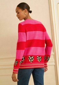 Pulover tricotat cu dungi în roșu și roz, având accente în formă de inimă cu imprimeu leopard la margine. Gât rotund, manșete lungi și cu tiv elastic.