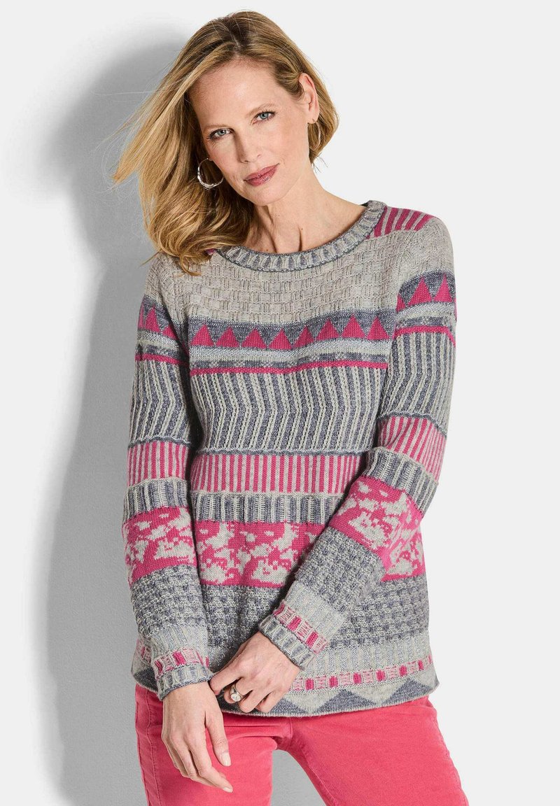 Grau gemusterter Pulli mit rosa und marineblauen Akzenten. Verfügt über geometrische Designs und strukturstrick, kombiniert mit rosa Hosen.