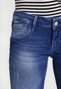 Denimjeans i medelblått med en blekt finish. Funktioner inkluderar en standard midja, framfickor och subtila slitningar.