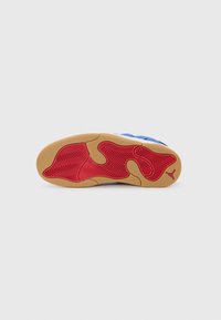 Semelle de chaussure de basketball avec une semelle en gomme présentant un motif de traction en chevrons rouges et une section supérieure bleue. Détail du logo subtil inclus.