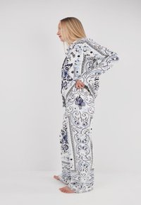 White pajama set featuring intricate blue and black floral patterns, with a long-sleeve hoodie and loose-fit pants. Soft fabric texture.