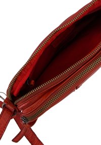 Rød læderhåndtaske med lynlås i toppen, der har en tekstureret overflade, foret med et matchende indre i rød stof, og som har et kompakt design.