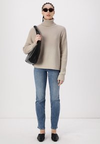 Jersey de cuello alto de canalé beige, jeans ajustados azul claro, bolso de bandolera negro y zapatos planos negros. Incluye mangas largas y un corte relajado.