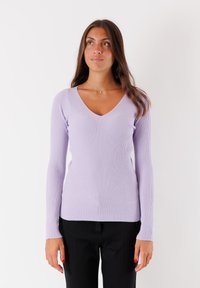 Top lungo a maniche con coste di colore lillà, design a V, caratterizzato da una silhouette aderente e un tessuto testurizzato. Indossato con pantaloni neri.
