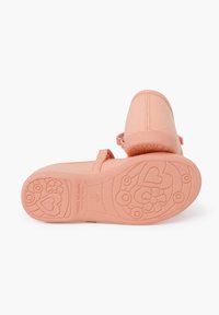 Zapatos de lona rosa con suela de goma texturizada que presenta patrones de flores y corazones. Correa ajustable para un ajuste seguro. Fabricado en España.