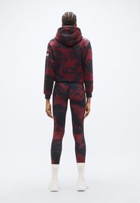 Prilegajo rdeče-črni vzorčasti pulover s kapuco z visokim ovratnikom in elastičnimi manšetami, v kombinaciji z usklajenimi legicami z istim vzorcem in dolžino do gležnjev.