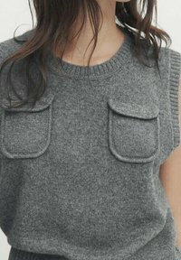 Pull sans manches en maille grise avec deux poches plaquées, col et ourlet côtelés. Texture douce, épaisseur moyenne.